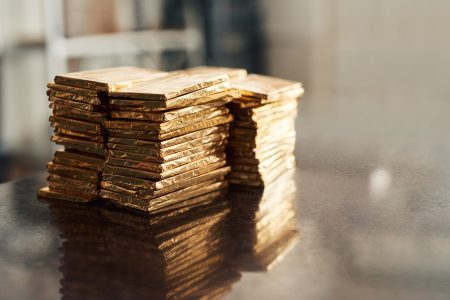 Closeup of stacks of prepared chocolate bars wrapped in gold foil sitting on a table in an artisanal chocolate making factory