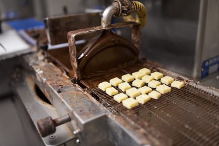 production, candy shop and industry concept - marzipan bars processing on chocolate coating machine at confectionery